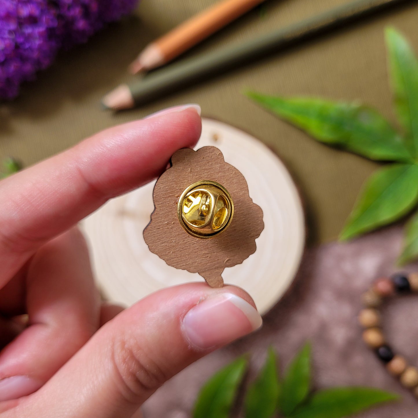 pins en bois d'une abeille mignonne posée sur une fleur orange avec un texte qui dit "Bee Kind". Fait à partir de bois éco responsable. Le pins est tenu dans la main, on voit le pins de dos, le bois brut de merisier et l'attache papillon dorée.