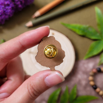 pins en bois d'une abeille mignonne posée sur une fleur orange avec un texte qui dit "Bee Kind". Fait à partir de bois éco responsable. Le pins est tenu dans la main, on voit le pins de dos, le bois brut de merisier et l'attache papillon dorée.